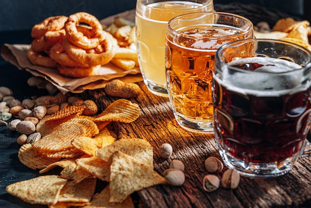 Drie glazen duur ambachtelijk bier, klassiek en ongefilterd en donker in een glas op tafel met een snack van pinda en pistache chips en nacho's