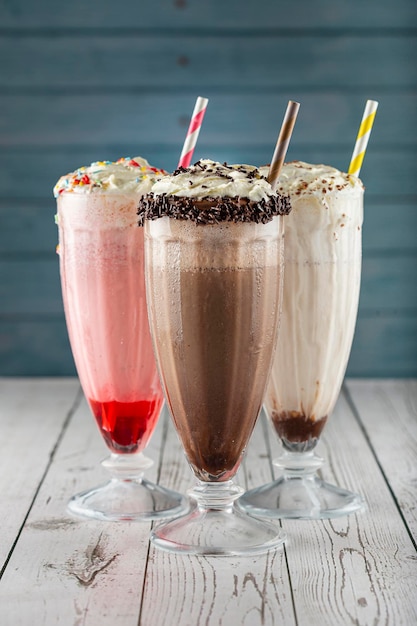 Foto drie glazen milkshake met diverse smaken. chocolade, vanille en aardbeienmilkshake.