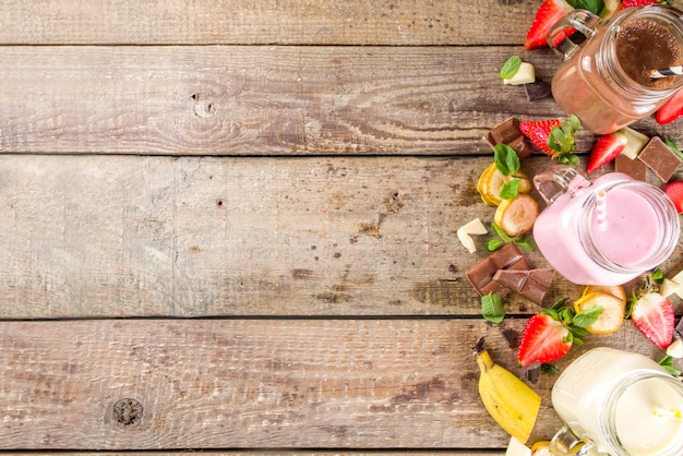 Foto drie glazen potten met milkshakes of smoothie. zomer gezond ontbijt, lunchdrankjes - milkshakes met banaan, chocolade en aardbeien