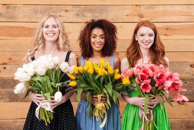 Foto drie glimlachende vrouwen die boeketten van bloemen tonen bij camera