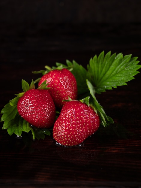 Drie grote aardbeien liggen op een donkere houten achtergrond. Laagdrempelig.