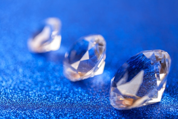 Drie grote dure diamanten die op de diagonaal op blauwe fonkelende lovertjesachtergrond worden gelegd, macro.