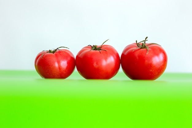 Drie grote rode sappige verse tomaten liggen op een groene tafel. Detailopname.