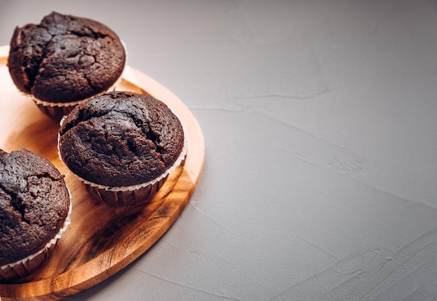 Drie heerlijke chocolademuffins op een houten bord op een grijze achtergrond