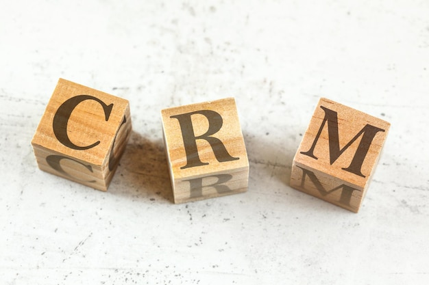 Drie houten kubussen met letters CRM - staat voor Customer Relationship Management - op wit bord.