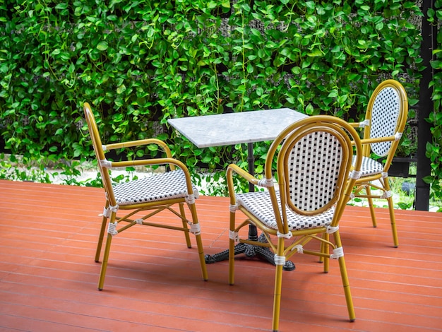 Drie houten witte vintage stoelen met witte marmeren tafel op rode vloer op groene klimop plant achtergrond