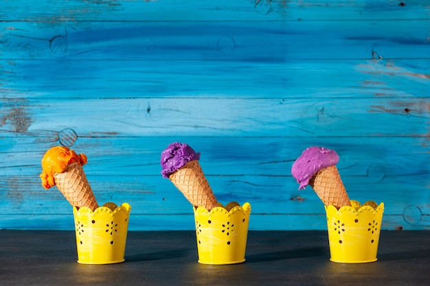 Drie ijshoorntjes op oude houten blauwe muur. de bolletjes zijn assorti van bosbessen-, aardbei- en abrikozenroomijs in wafels