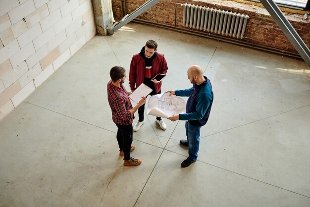 Drie jonge architecten bespreken details van schets en andere punten van een nieuw project terwijl ze brainstormen, ideeën uitwisselen en overleggen