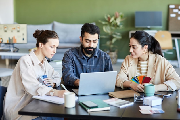 Drie jonge creatieve ontwerpers met paletten kijken naar online training over trendy kleuren en discus