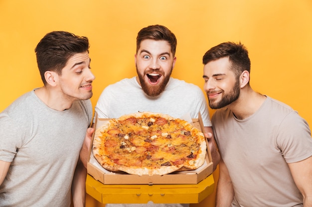 Drie jonge glimlachende mannen die een grote pizza ruiken