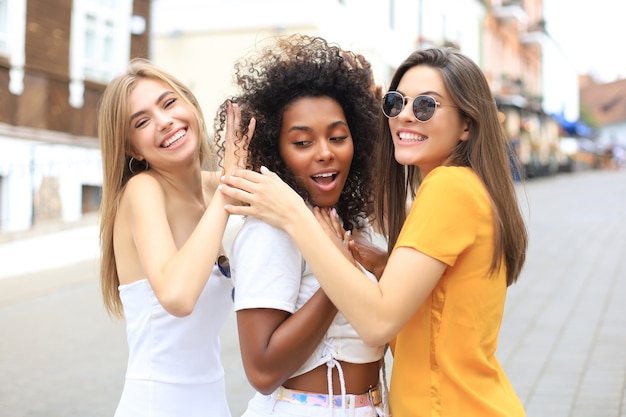 Drie jonge lachende hipster vrouwen in zomer kleding poseren op straat. Vrouw positieve gezicht emoties tonen.