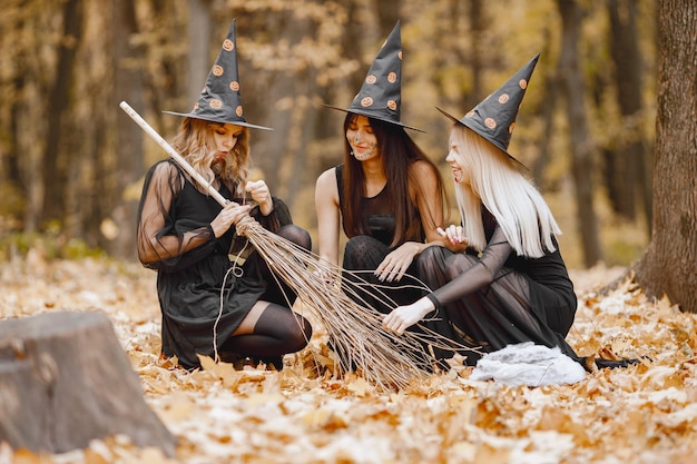 Drie jonge meisjesheksen in bos op Halloween. Meisjes dragen zwarte jurken en kegelhoed. Heks die een bezem vasthoudt.