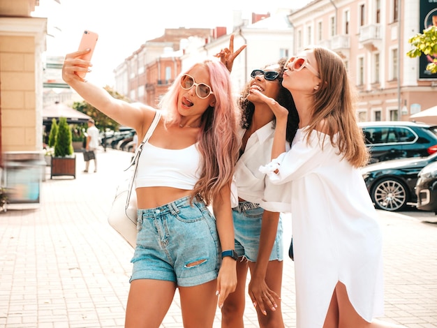 Drie jonge mooie lachende vrouw in trendy zomerkleren sexy zorgeloze multiraciale vrouwen poseren op de straat achtergrond positieve modellen plezier in zonnebril vrolijk en gelukkig