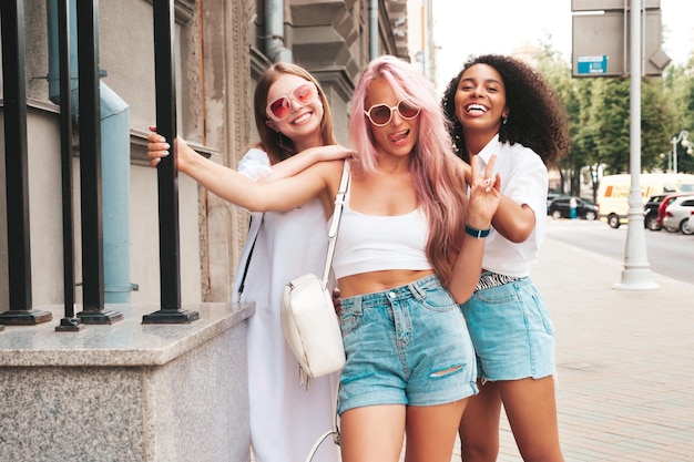 Foto drie jonge mooie lachende vrouw in trendy zomerkleren sexy zorgeloze multiraciale vrouwen poseren op de straat achtergrond positieve modellen plezier in zonnebril vrolijk en gelukkig