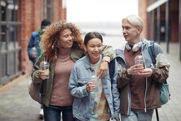 Drie jonge vrolijke vrienden in vrijetijdskleding met drankjes op weg naar huis