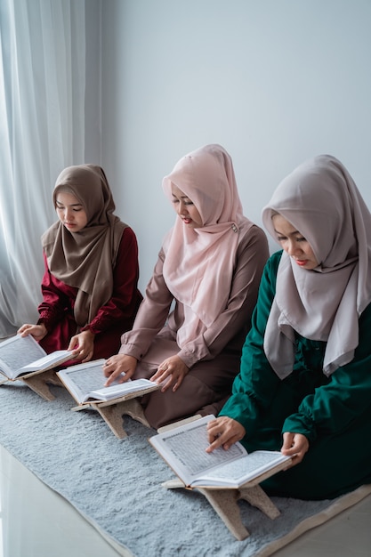 Drie jonge vrouwen die hijabs dragen, lezen samen het heilige boek van de al-quran