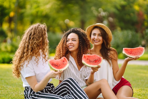 Drie jonge vrouwen hebben samen plezier en eten watermeloen op hete zomerdag