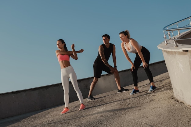 Drie jongeren in sportkleding verwarmen zich voor ze samen buiten trainen.