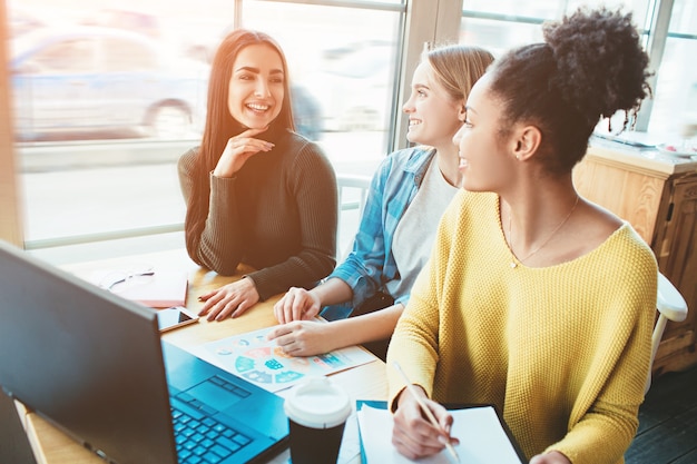 Drie kameraden zitten samen aan dezelfde tafel in het café en kijken naar het scherm van de laptop