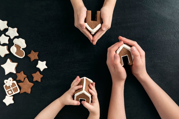 Drie kinderen houden peperkoekhuisjes vast. Bovenaanzicht op zwarte achtergrond.