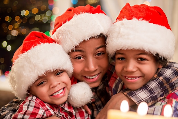 Drie kinderen in kerstmutsen. glimlachende afrojongens op kerstmis. drie gelukkige broers op vakantie. kerstavond in het familiehuis.
