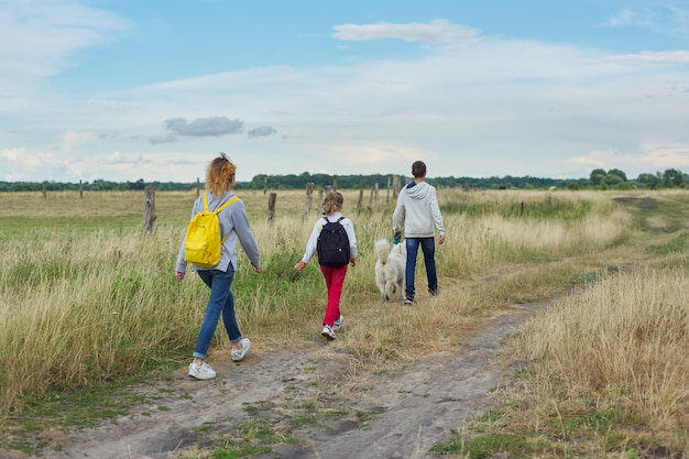 Drie kinderen met hond wandelen langs landweg, uitzicht vanaf de achterkant