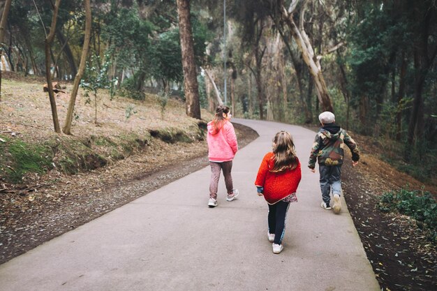 Drie kinderen trekken meisjes en een jongen lopend en pratend in een parkweg