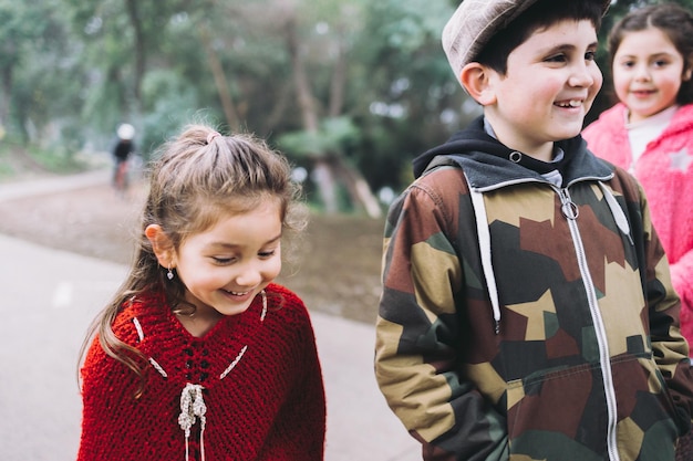 Drie kinderen, twee meisjes en een jongen die in een parkweg lopen en praten