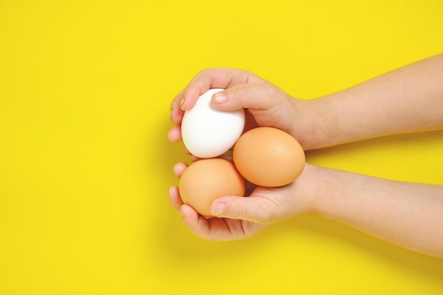 Drie kippeneieren in de handen van een jongen op een gele achtergrond.