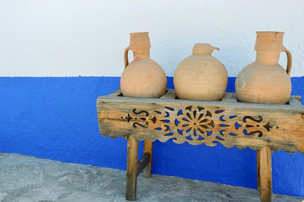 Foto drie klassieke kleipotten die zich op houten lijst bevinden, gesneden artistiek ornament tegen blauwwitte muur