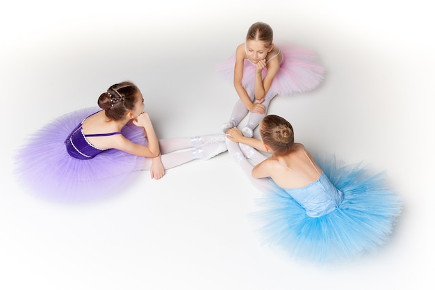 Drie kleine balletmeisjes die in tutu zitten en samen poseren