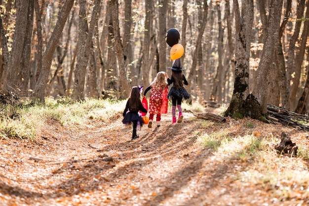 Drie kleine meisjes in heksenkostuums lachen lachend door het herfstbos met manden voor snoep