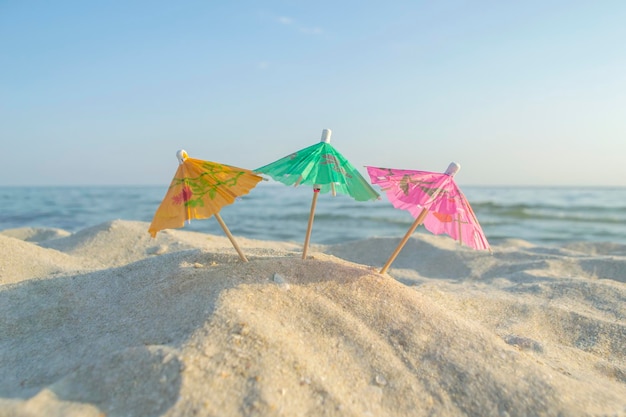 Drie kleine papieren cocktailparaplu's staan in zand op zandstrand close-up