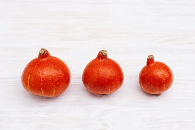 Drie kleine pompoenen in rij op witte houten achtergrond