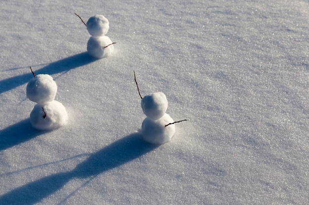 Drie kleine sneeuwpoppen in het winterseizoen, de sneeuwpop is gemaakt van verschillende onderdelen en staat in de sneeuw bij koud weer, spelletjes in de sneeuw met het maken van verschillende sneeuwpopfiguren