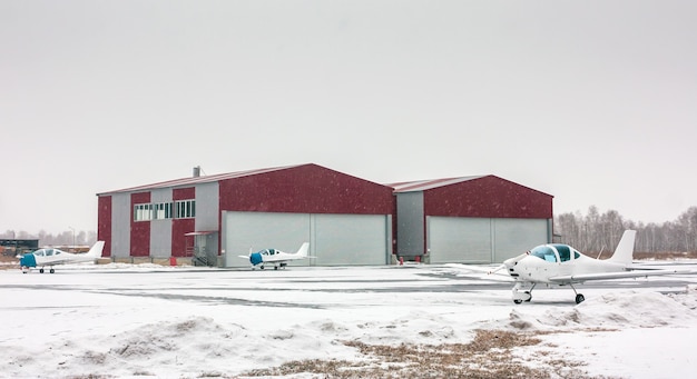 Drie kleine sportvliegtuigen naast een hangar op het wintervliegveld