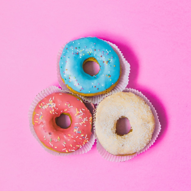 Drie kleurrijke ronde donuts op roze achtergrond