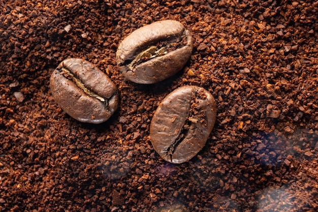 Drie koffiebonen liggen op gemalen koffie close-up