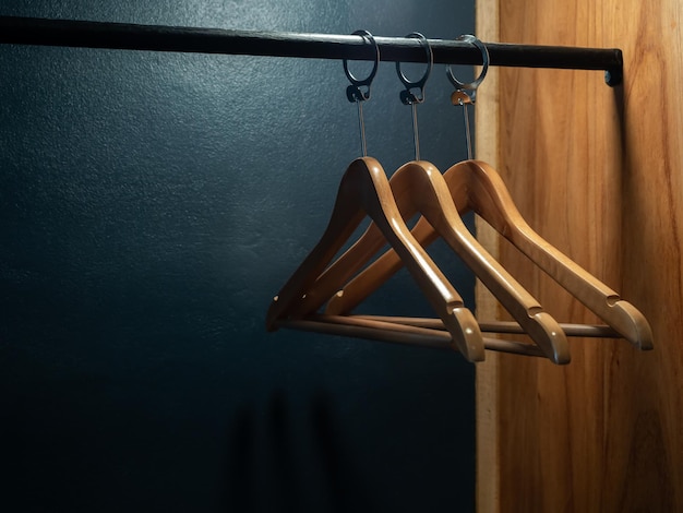 Drie lege houten kleerhangers zonder overhemden of jurk hangen aan een zwart stoffen rek in de houten kledingkast op donkerblauwe achtergrond ter voorbereiding op de gast die in de kamer in het hotel verblijft