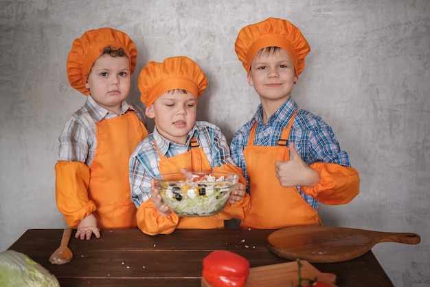 Drie leuke Europese jongens in oranje kostuums koken koken een salade van groenten. een familiediner koken