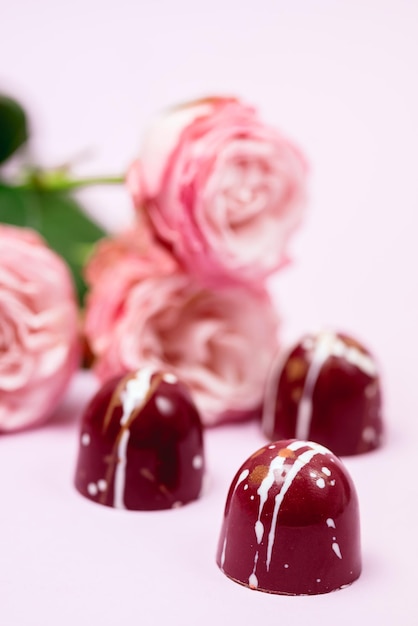 Drie luxe bonbons geschilderd met witte kleuren op roze achtergrond Mooie en exclusieve handgemaakte chocoladesuikergoed en rozenbloemen verticaal