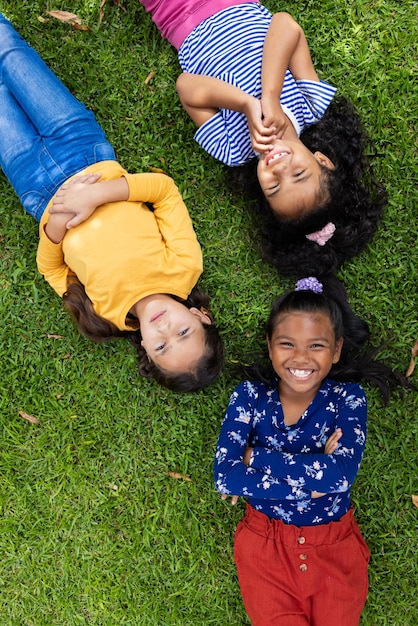 Drie meisjes van verschillende rassen liggen op het gras in de school en glimlachen en kijken omhoog.