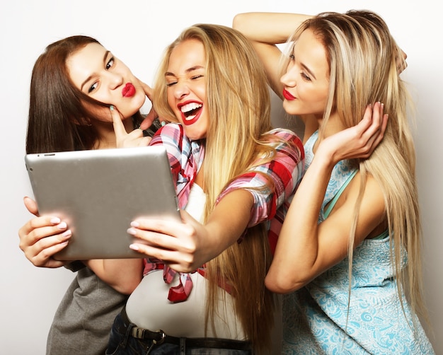 Drie meisjesvrienden die selfie met digitale tablet nemen, op grijs