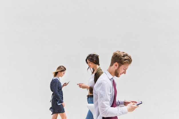 Drie mensen die tegen witte achtergrond lopen die mobiele telefoon met behulp van