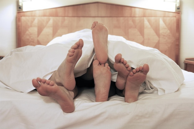 Drie mensen onder een deken op bed.