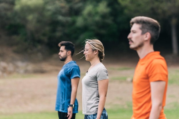 Drie mensen staan yoga te doen in een park tijdens winderige dag