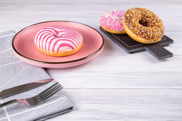 Drie met suiker bedekte donuts liggen op een roze keramische plaat en een leistenen bord Serveren met bestek en linnen servet Selectieve aandacht Kopieerruimte
