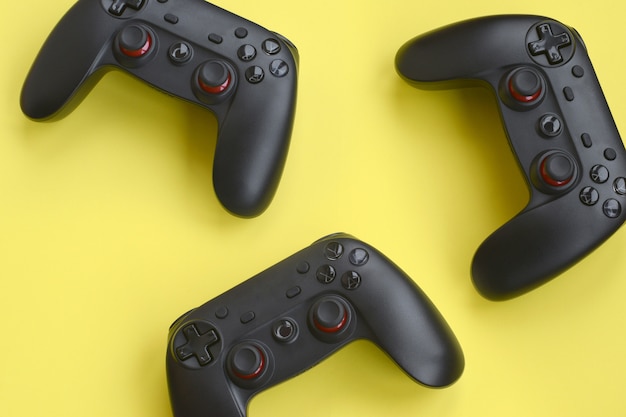 Drie moderne zwarte gamepads op gele achtergrond. Laten we videogames spelen samen met vriendenconcept. Coöperatief teamspel