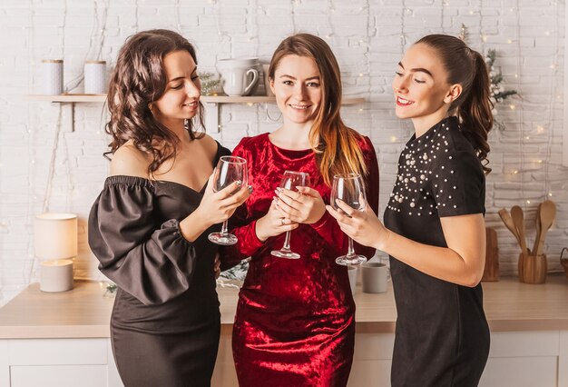 Drie mooie vrolijke gelukkige jonge meisjes vriend lachen met een glas alcohol aan de kerst eettafel op de achtergrond van de keuken van het nieuwe jaar