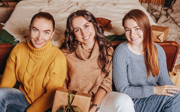 Drie mooie vrolijke gelukkige jonge meisjes vriendin geven kerstcadeaus op de achtergrond van een nieuwe jaarboom thuis